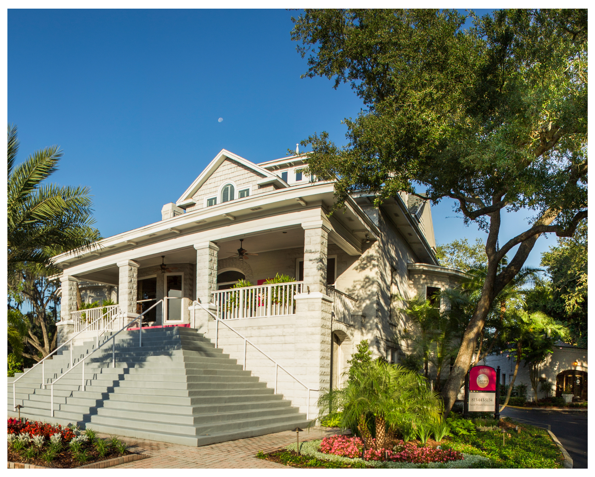 The Bigelow Mansion at 4807 Bayshore Blvd: a grey stone porch with wide steps under palms and a live oak, with the Faces sign by the drive
